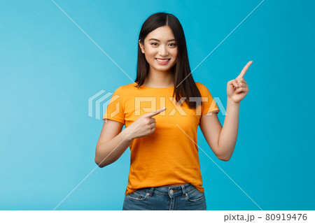Friendly cheerful asian brunette girl inviting visit link interesting place, pointing upper right corner smiling joyfully camera, telling you about good promotion, stand blue background upbeat 80919476