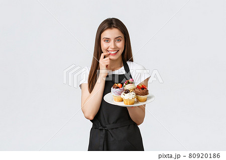 Grocery store employees, small business and coffee shops concept. Cheerful silly waitress want have bite of delicious cupcakes. Barista biting lip tempting to taste new desserts, white background Grocery store employees, small business and coffee shops concept. Cheerful silly waitress want have bite of delicious cupcakes. Barista biting lip tempting to taste new desserts, white background 80920186