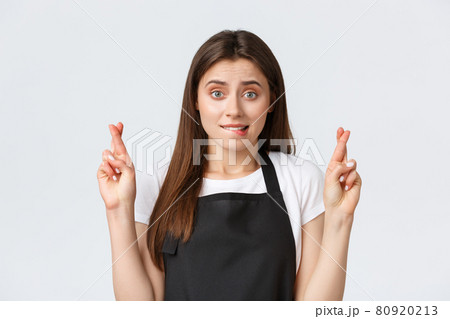 Employees, job employment, small business and coffee shop concept. Nervous cute cafe worker, saleswoman in black apron biting lip worried and cross fingers good luck, making wish, waiting for results 80920213