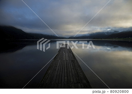 立ち込む雲が映りこんだ静かな朝の湖に伸びる一本の木製桟橋 立ち込む雲が映りこんだ静かな朝の湖に伸びる一本の木製桟橋 80920800