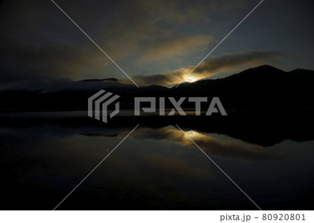 雲と山並のシルエットが水鏡に映りこんでいる湖に対岸の稜線を超えた朝陽が届き始める 80920801