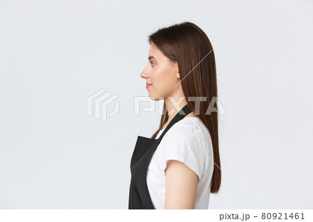 Employees, job employment, small business and coffee shop concept. Profile of friendly-looking smiling barista, cafe worker in black apron serving orders to customers, looking left Employees, job employment, small business and coffee shop concept. Profile of friendly-looking smiling barista, cafe worker in black apron serving orders to customers, looking left 80921461