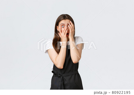 Grocery store employees, small business and coffee shops concept. Scared insecure female barista in black apron cover face terrified, peeking though fingers with fear, standing white background 80922195