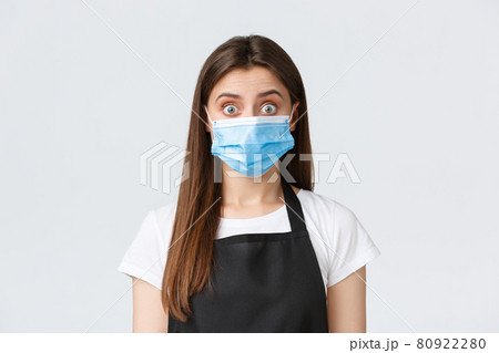 Covid-19 social distancing, cafe employees, coffee shops and coronavirus concept. Shocked and surprised cute brunette barista in medical mask widen eyes as hear gossip or big news 80922280