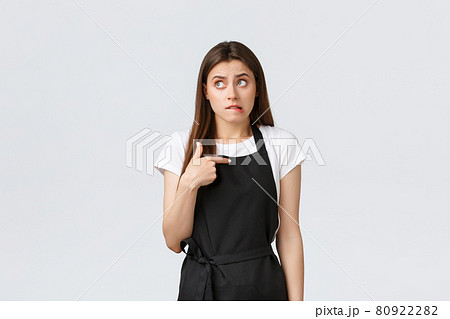 Grocery store employees, small business and coffee shops concept. Anxious cute female barista biting lip awkward, looking up pondering and pointing herself doubtful, wearing black apron uniform Grocery store employees, small business and coffee shops concept. Anxious cute female barista biting lip awkward, looking up pondering and pointing herself doubtful, wearing black apron uniform 80922282
