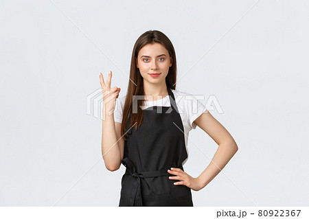 Grocery store employees, small business and coffee shops concept. Smiling friendly cafe worker in black apron showing two with fingers. Waitress telling order number, white background 80922367