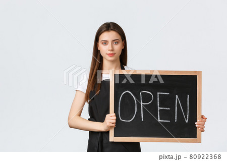 Grocery store employees, small business and coffee shops concept. Cute young female shop worker in black apron holding we are open sign, inform guests cafe is working, white background 80922368