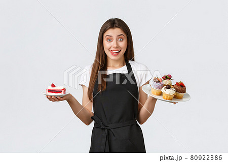 Grocery store employees, small business and coffee shops concept. Friendly smiling waitress in cafe holding plates with cupcakes and cafe, serving desserts for guests, standing white background 80922386
