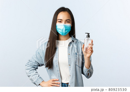 Social distancing lifestyle, covid-19 pandemic preventing virus concept. Young cute asian female in medical mask advice using hand sanitizer, showing soap bottle, explain measures during coronavirus Social distancing lifestyle, covid-19 pandemic preventing virus concept. Young cute asian female in medical mask advice using hand sanitizer, showing soap bottle, explain measures during coronavirus 80923530