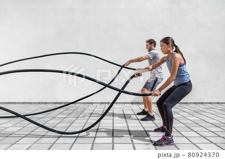 Fitness people exercising with battle ropes at gym. Woman and man couple training together doing battling rope workout working out arms and cardio for crossfit exercises Fitness people exercising with battle ropes at gym. Woman and man couple training together doing battling rope workout working out arms and cardio for crossfit exercises 80924370