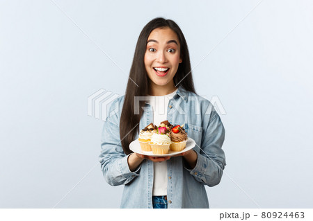Social distancing lifestyle, covid-19 pandemic, celebrating holidays during coronavirus concept. Excited asian girl holding plate with tasty cupcakes, smiling broadly, invite visit cafe with muffins Social distancing lifestyle, covid-19 pandemic, celebrating holidays during coronavirus concept. Excited asian girl holding plate with tasty cupcakes, smiling broadly, invite visit cafe with muffins 80924463