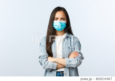 Social distancing lifestyle, covid-19 pandemic life and leisure concept. Suspicious and disappointed young girl in medical mask, asian female looking displeased, cross arms chest and frowning Social distancing lifestyle, covid-19 pandemic life and leisure concept. Suspicious and disappointed young girl in medical mask, asian female looking displeased, cross arms chest and frowning 80924467