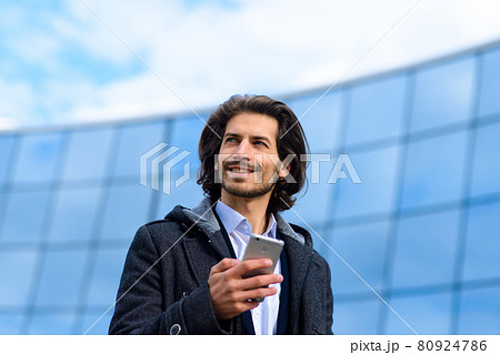 Modern confident young businessman in full suit standing outdoors with cityscape in the background 80924786