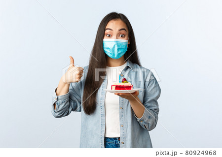 Social distancing lifestyle, covid-19 pandemic, celebrating holidays during coronavirus concept. Happy smiling asian birthday girl in medical mask, show bday cake and thumb-up pleased 80924968