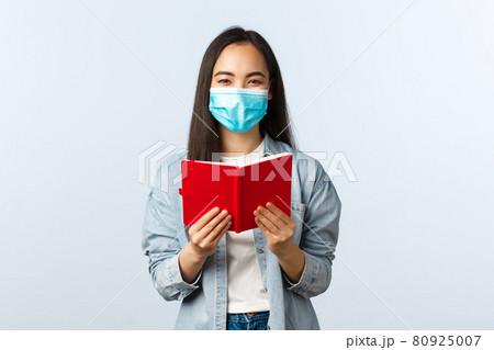 Covid-19 pandemic, education during coronavirus, back to school concept. Cheerful friendly smiling asian woman in medical mask prepare for college exam, studying notes in notebook 80925007