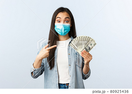 Social distancing lifestyle, covid-19 pandemic business and employement concept. Excited female asian employee suggest you earn lots money, pointing at cash dollars, wear medical mask Social distancing lifestyle, covid-19 pandemic business and employement concept. Excited female asian employee suggest you earn lots money, pointing at cash dollars, wear medical mask 80925436