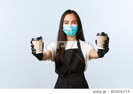 Covid-19, social distancing, small coffee shop business and preventing virus concept. Smiling friendly female barista, asian cafe owner in medical mask and gloves handing order, two cups of drinks 80926254