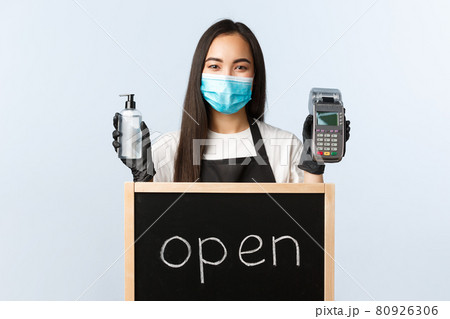 Small business, covid-19 pandemic, preventing virus and contactless orders concept. Cute asian female barista or waitress with we are open sign, showing hand sanitizer and paying terminal Small business, covid-19 pandemic, preventing virus and contactless orders concept. Cute asian female barista or waitress with we are open sign, showing hand sanitizer and paying terminal 80926306