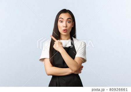 Coffee shop, small business and startup concept. Surprised and amazed young cute asian barista in black apron telling interesting news, pointing finger upper left corner, look interested 80926661