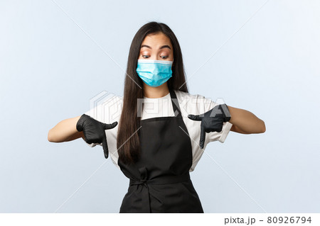 Covid-19 pandemic, social distancing, small business and preventing virus concept. Intrigued and curious asian coffee shop barista, employee in medical mask and gloves peeking down, pointing bottom Covid-19 pandemic, social distancing, small business and preventing virus concept. Intrigued and curious asian coffee shop barista, employee in medical mask and gloves peeking down, pointing bottom 80926794
