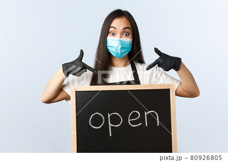 Small business, covid-19 pandemic, preventing virus and employees concept. Excited cute asian female barista, cafe or store worker in medical mask pointing at we are open sign Small business, covid-19 pandemic, preventing virus and employees concept. Excited cute asian female barista, cafe or store worker in medical mask pointing at we are open sign 80926805