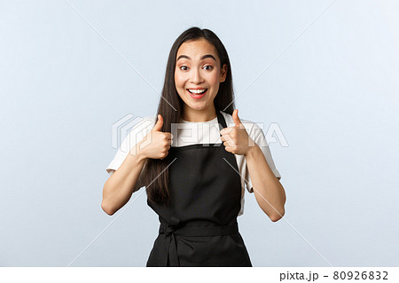 Coffee shop, small business and startup concept. Excited smiling asian waitress approve new menu. Cute female barista in black apron show thumbs-up in support, like or agree Coffee shop, small business and startup concept. Excited smiling asian waitress approve new menu. Cute female barista in black apron show thumbs-up in support, like or agree 80926832