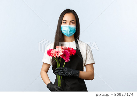 Small business, coronavirus pandemic, orders and shops concept. Smiling cute asian female florist in medical mask, holding bouquet for customer, selling flowers during covid-19 outbreak Small business, coronavirus pandemic, orders and shops concept. Smiling cute asian female florist in medical mask, holding bouquet for customer, selling flowers during covid-19 outbreak 80927174