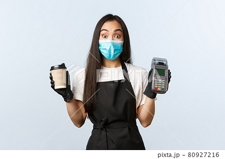 Coffee shop, coronavirus, social distancing and contactless payment concept. Surprised asian waitress, barista at cafe in medical mask and gloves with coffee order and POS terminal 80927216
