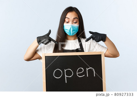 Small business, covid-19 pandemic, preventing virus and employees concept. Excited cute asian female barista, cafe or store worker in medical mask pointing at we are open sign Small business, covid-19 pandemic, preventing virus and employees concept. Excited cute asian female barista, cafe or store worker in medical mask pointing at we are open sign 80927333