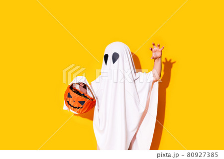 Child in ghost costume holding pumpkin basket Halloween trick or treat Child in ghost costume holding pumpkin basket Halloween trick or treat 80927385
