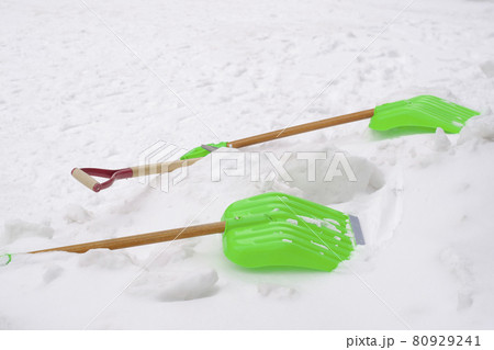 Two green reflective plastic shovels placed in white snowflakes 80929241