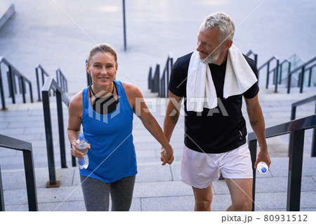 Attractive middle aged couple of sportive man and woman looking happy, holding hands while walking up the stairs after training together in the city Attractive middle aged couple of sportive man and woman looking happy, holding hands while walking up the stairs after training together in the city 80931512