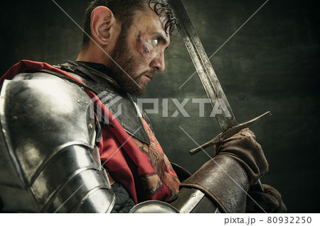 Side view. Portrait of one brutal bearded man, medeival warrior or knight with dirty wounded face holding sword Side view. Portrait of one brutal bearded man, medeival warrior or knight with dirty wounded face holding sword 80932250