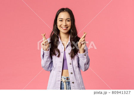 Portrait of excited attractive young korean girl having faith everything be good, keep fingers crossed while making wish, dreaming about desire come true, pink background 80941327