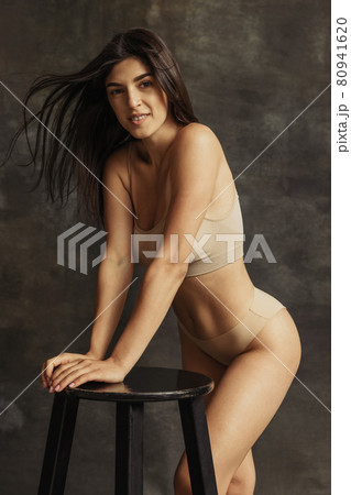 Portrait of young beautiful tanned woman in lingerie posing isolated over dark vintage studio background. Natural beauty concept. 80941620