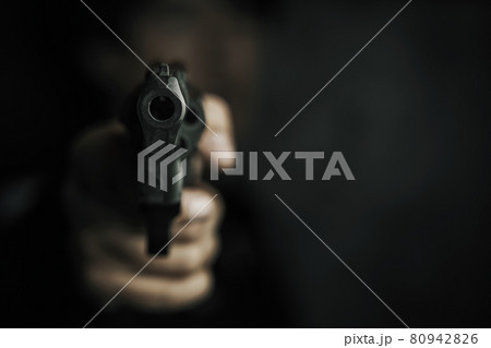 Muzzle of gun in man's hand is pointed at camera. 80942826