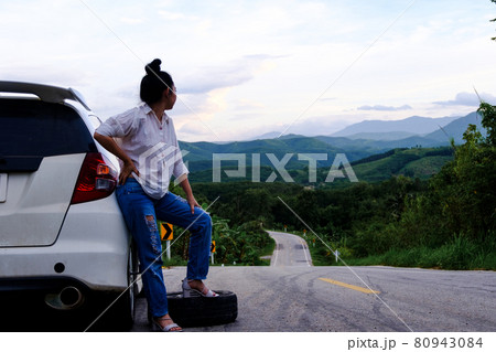 Young woman hitchhiking on the road on the public road in the forest area at mountain and sky background 80943084