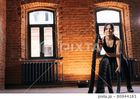 Focused fitness young athletic woman with strong beautiful body in black sportswear exercising with battle ropes having workout training. Focused fitness young athletic woman with strong beautiful body in black sportswear exercising with battle ropes having workout training. 80944165