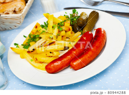Appetizing sausages with potatoes and pickled cucumbers closeup 80944288