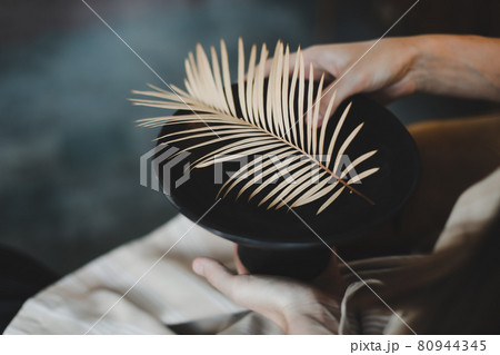 female hands holding a black ceramic plate decorated with fern leaf close-up female hands holding a black ceramic plate decorated with fern leaf close-up 80944345