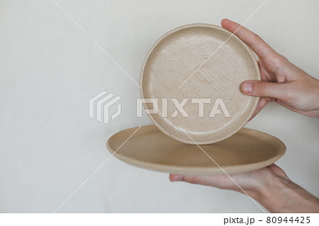 Hands holding ceramic plates isolated on white background. Minimalist set of handmade ceramic tableware and pottery 80944425