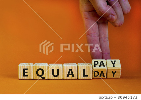 Equal pay day symbol. Businessman turns wooden cubes and changes words equal pay to equal day. Beautiful orange background. Copy space. Business and equal pay day concept. Equal pay day symbol. Businessman turns wooden cubes and changes words equal pay to equal day. Beautiful orange background. Copy space. Business and equal pay day concept. 80945173