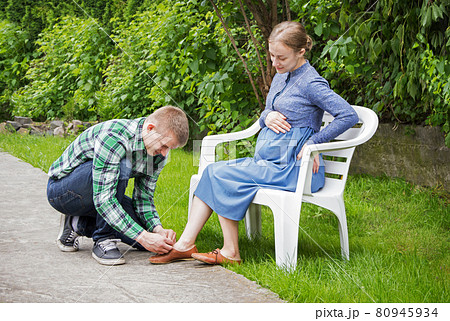 Husband ties the laces on the shoes of his pregnant wife 80945934