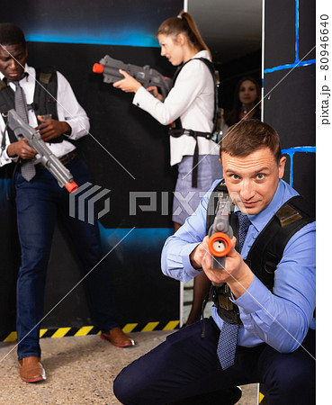 Men and women in business suits playing laser tag emotionally in dark room Men and women in business suits playing laser tag emotionally in dark room 80946640