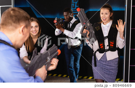 Men and women in business suits playing laser tag emotionally in dark room 80946669