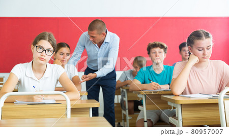 Focused teenage students studying in classroom with teacher, writing lectures in workbooks 80957007