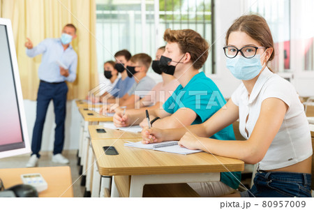 Teenage girl in protective mask studying in college with classmates 80957009