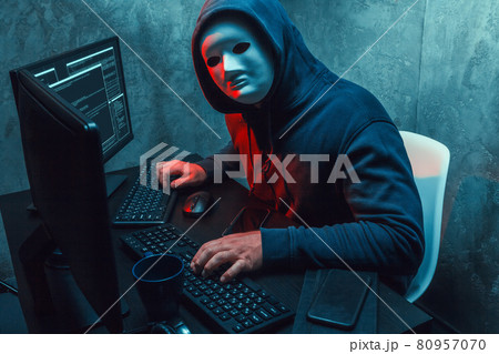 Anonymous hacker wearing face mask working on computer in dark room Anonymous hacker wearing face mask working on computer in dark room 80957070