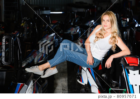 Cheerful young caucasian woman near racing cars at kart circuit Cheerful young caucasian woman near racing cars at kart circuit 80957071