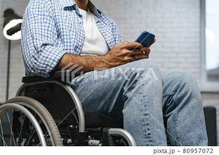 Mixed raced disabled man sitting in a wheelchair and using smartphone Mixed raced disabled man sitting in a wheelchair and using smartphone 80957072